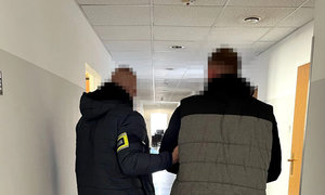 poszukiwany mężczyzna w asyście nieumundurowanego policjanta stojący na korytarzu