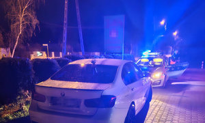 auto zatrzymane do kontroli drogowej, w tle policyjny radiowóz na sygnałach
