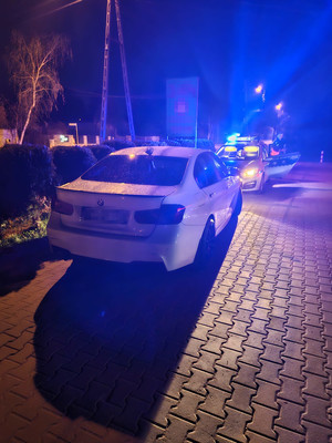 auto zatrzymane do kontroli drogowej, w tle policyjny radiowóz na sygnałach