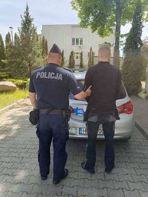 mężczyzna a umundurowanym policjantem, obydwoje stoją tyłem, w tle policyjny radiowóz