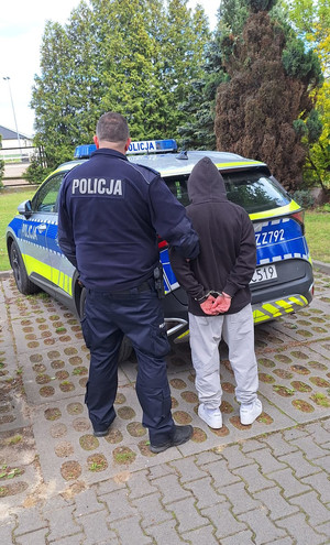 zatrzymany mężczyzna w asyście policjanta, w tle radiowóz