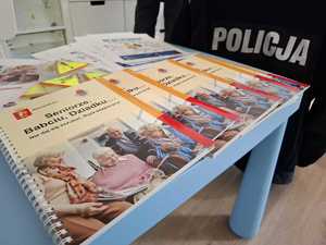 ulotki nie daj się oszukać leżące na stoliku, w tle napis policja