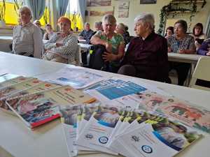 ulotki nie daj się oszukać leżące na stoliku, w tle siedzący seniorzy