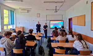 uczniowie siedzą w ławkach szkolnych, policjanci stoją przed nimi, w tle wyświetlana jest prezentacja dotycząca odpowiedzialności prawnej nieletnich