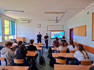 uczniowie siedzą w ławkach szkolnych, policjanci stoją przed nimi, w tle wyświetlana jest prezentacja dotycząca odpowiedzialności prawnej nieletnich