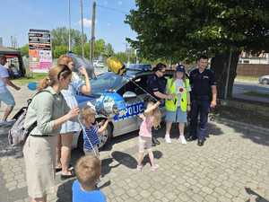 policjanci wspólnie z dziećmi, w tle policyjny radiowóz