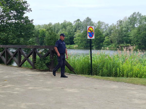 dzielnicowy idący na kontrolę dzikich kąpielisk, znak "zakaz kąpieli" w tle