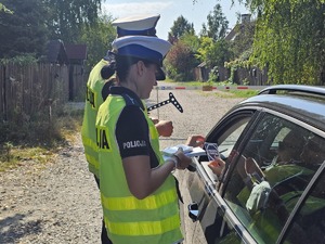 policjanci kontrolujący prędkość, policjantka trzyma ulotki akcji "Mistrzu zwolnij"
