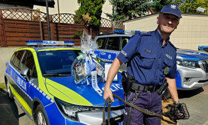 st. asp. Sławomir Matyjasiak wspólnie z psem słuzbowym, w tle radiowóz