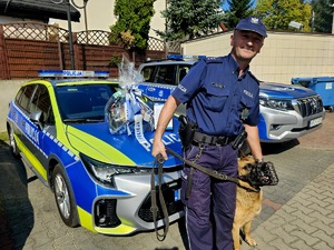 st. asp. Sławomir Matyjasiak wspólnie z psem słuzbowym, w tle radiowóz