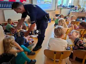 policjant pokazujący dzieciom różnicę widoczności osoby w odblaskach oraz tej która ich nie nosi