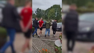 nieumundurowani policjanci prowadzący zatrzymanych mężczyzn, w tle policyjny nieoznakowany radiowóz