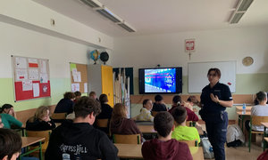 policjantka prowadząca spotkanie z uczniami, w tle wyświetlana jest prezentacja