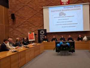 zdjęcie z debaty społecznej, sala konferencyjna. Przy stolikach siedzą przedstawiciele mieszkańców, urzędu, a także policjanci