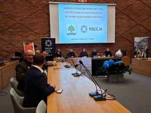 zdjęcie z debaty społecznej, sala konferencyjna. Przy stolikach siedzą przedstawiciele mieszkańców, urzędu, a także policjanci