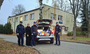 policjanci stojący przy radiowozie, w bagażniku produkty zebrane w ramach szlachetnej paczki