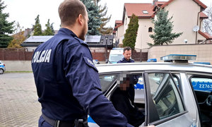 zatrzymany mężczyzna siedzący w radiowozie, obok niego stoją umundurowani policjanci