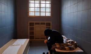 mężczyzna ubrany na czarno w celi dla osób zatrzymanych