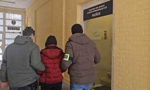 nieumundurowani policjanci prowadzący zatrzymanego nieletniego, w tle wejście do Policyjnej Izby Dziecka
