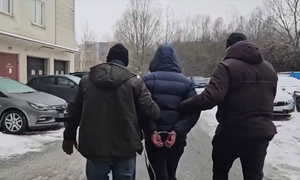 nieumundurowani policjanci z zatrzymanym mężczyzną, na dziedzińcu jednostki