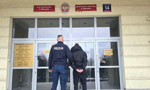 zatrzymany mężczyzna w asyście nieumundurowanego policjantka, w tle wejście do budynku Prokuratury Rejonowej w Piasecznie