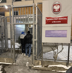 zatrzymany mężczyzna w asyście nieumundurowanego policjanta przy wejściu do Placówki Straży Granicznej w Warszawie