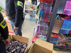 nieumundurowani policjanci z opaskami "Policja" na ramieniu, w tle boks sklepowy z towarem, kartony