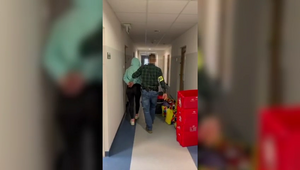 nieumundurowany policjant z zatrzymaną kobietą z kajdankami założonymi na ręce trzymane z tyłu, zdjęcie wykonane w korytarzu jednostki