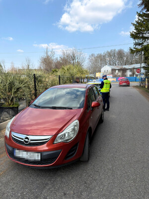 kontrola drogowa. Policjant rozmawiający z kierującym, w tle czerwony Opel Corsa oraz oznakowany policyjny radiowóz