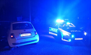 policyjny oznakowany radiowóz z włączonymi sygnałami świetlnymi, obok stojące auto zatrzymane do kontroli drogowej