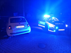 policyjny oznakowany radiowóz z włączonymi sygnałami świetlnymi, obok stojące auto zatrzymane do kontroli drogowej