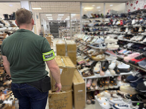 nieumundurowany policjant z opaską odblaskową z napisem POLICJA. W tle zablurowany zabezpieczony towar