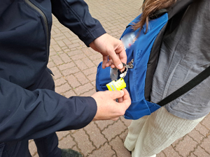 Umundurowana policjantka przyczepia plecaka szkolnego element odblaskowy. Plecak ma na sobie uczeń.