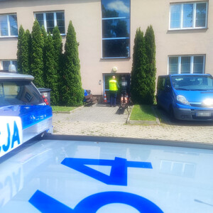 policjant piaseczyńskiej drogówki wraz z zatrzymanym mężczyzną, w tle budynek Komisariatu Policji