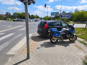 policyjny oznakowany motocykl a obok niego auto zaparkowane obok przejścia dla pieszych