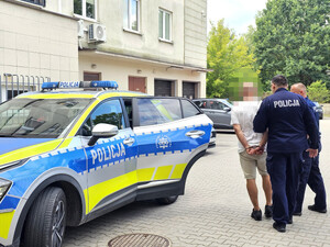 zatrzymany mężczyzna w trakcie doprowadzania do policyjnego radiowozu przez umundurowanych policjantów