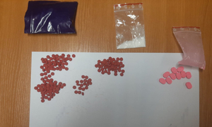 Na stole są trzy woreczki strunowe. w jednym jest biały proszek. Pod nimi na białej kartce papieru są pogrupowane tabletki różnego koloru.