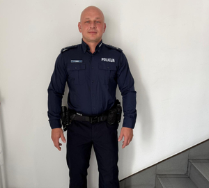 Umundurowany policjant stoi pod ścianą.