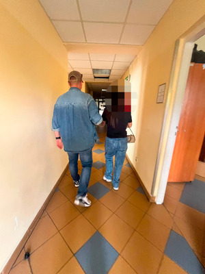 zatrzymana kobieta w asyście nieumundurowanego policjanta, zdjęcie wykonane na korytarzu