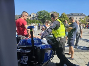 policjant przy policyjnym motocyklu, obok niego uczestnicy pikniku