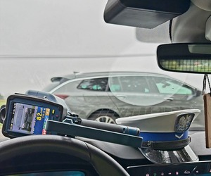 urządzenie do pomiaru prędkości z wynikiem pomiaru, leżące na podszybiu auta. W tle widoczna czapka policjanta ruchu drogowego, jak również kontrolowane auto