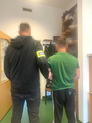 zatrzymany mężczyzna w asyście nieumundurowanego policjanta, który ma na ramieniu opaskę odblaskową z napisem POLICJA