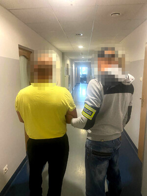 zatrzymany mężczyzna w asyście nieumundurowanego policjanta, który ma na ramieniu opaskę odblaskową z napisem POLICJA