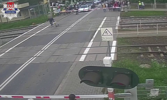 mężczyzna prowadzący hulajnogę elektryczną, przechodzący przez przejazd kolejowo-drogowy, kiedy zapory były opuszczone